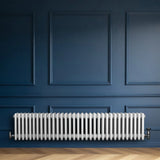 Traditional white 4 column radiator with valves, featuring a sleek design against a deep blue wall and wooden floor