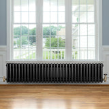 Traditional black 4 column radiator with brass valves, positioned under a large window, enhancing a bright, airy room with wooden flooring