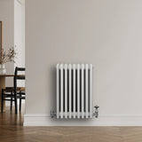 Traditional white 4 column radiator with smooth, glossy finish and chrome valves, mounted on a light-colored wall in a modern interior