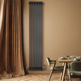 Tall anthracite grey traditional 4 column radiator with valves, mounted on a warm-toned wall, beside a cozy dining area