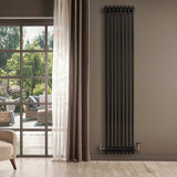Traditional black 4 column radiator with brass valves, mounted on a wall beside large windows, enhancing a modern interior space