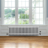 Traditional white 4 column radiator with valves, featuring a sleek design and smooth finish, positioned under a large window