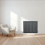 Flat single column radiator in anthracite grey, featuring vertical slats, sleek design, and positioned beside a modern armchair in a bright room