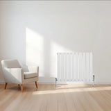Flat single column radiator in white, 600mm x 700mm, with sleek vertical bars, positioned beside a modern armchair in a bright room
