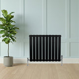 Flat black single column radiator, 600 x 700mm, featuring sleek vertical slats, positioned against a light blue wall with a plant nearby