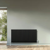 Sleek black oval single column radiator, 600 x 1200mm, mounted on a light gray wall, complementing a modern interior design