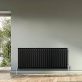 Sleek black oval single column radiator, 600 x 1440mm, mounted on a wall with a modern interior and natural light streaming in
