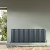 Oval single column radiator in anthracite grey, 600 x 1620mm, featuring a sleek design with vertical fins, set against a light wall and wooden floor