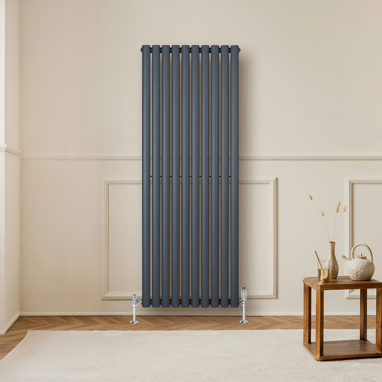 Oval single column radiator in anthracite grey, featuring vertical bars, sleek design, and mounted against a light wall in a modern room setting