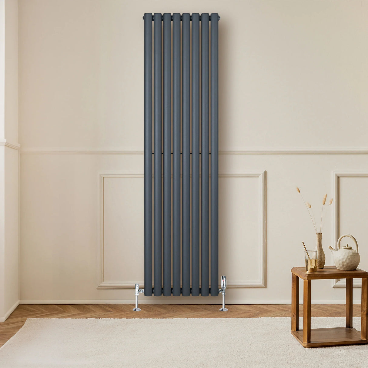 Anthracite grey oval single column radiator, 1800 x 480mm, mounted on a light wall, paired with a wooden table and decor elements