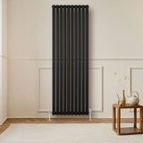 Sleek black oval single column radiator, 1800 x 600mm, mounted on a light wall, complementing a modern interior with wooden flooring