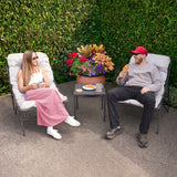 Stylish grey 3 piece bistro set featuring two cushioned chairs and a small table, set against vibrant greenery and colorful flowers