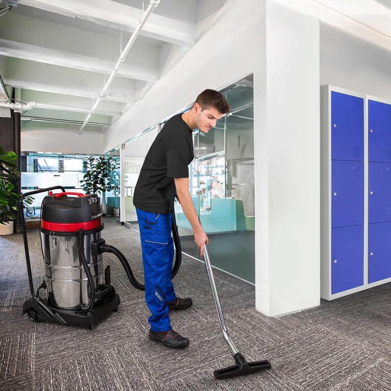 A young man in a black shirt and blue pants uses a commercial vacuum cleaner on a carpeted office floor with lockers in the background