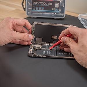 Precision screwdriver set in use, featuring a red handle, opening a smartphone with visible internal components and tools