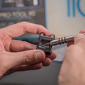 Precision screwdriver set with a sleek metal handle and interchangeable tips, held in a hand against a blurred background