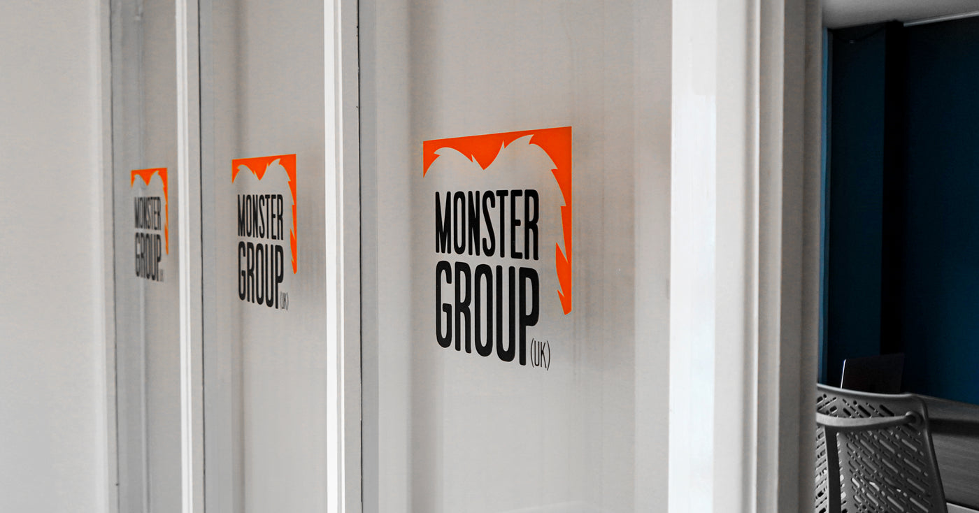 Bold orange and black logo of Monster Group displayed on a glass door, featuring modern typography and a sleek design