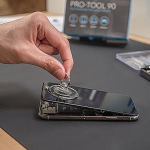 Precision screwdriver set in use, removing a smartphone screen with a suction cup tool on a black work surface, showcasing versatility