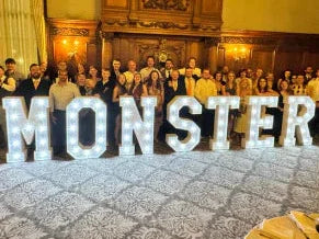 Group of people in a formal setting with large letter blocks spelling 'MONSTER'.
