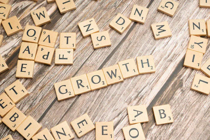 Wooden Scrabble tiles scattered on a rustic wooden surface, with the word "GROWTH" prominently displayed in the center